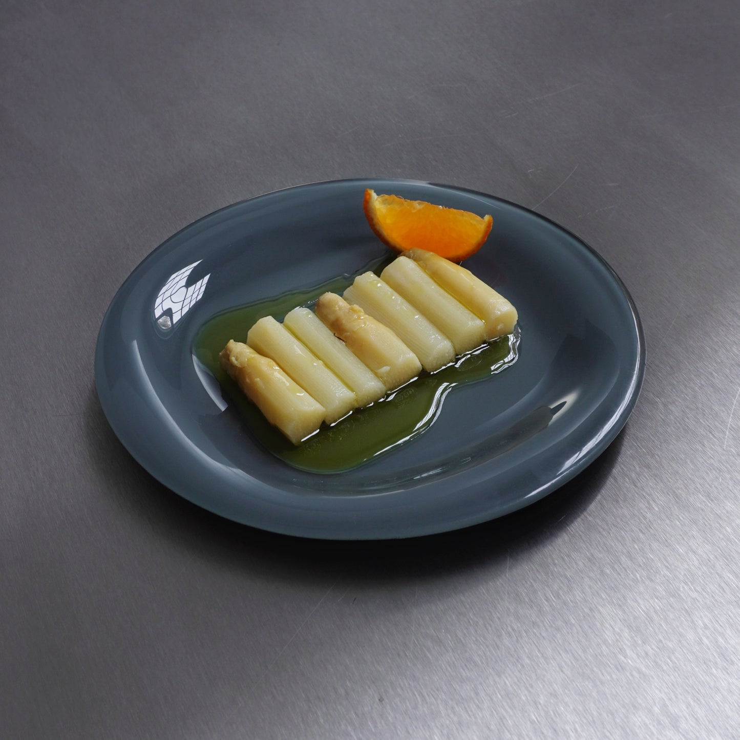 White asparagus in oil with an orange slice on a slate grey glass dinner plate